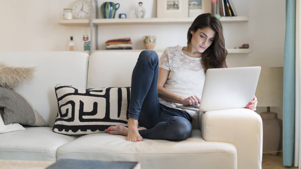 Woman sitting on couch at home using laptop